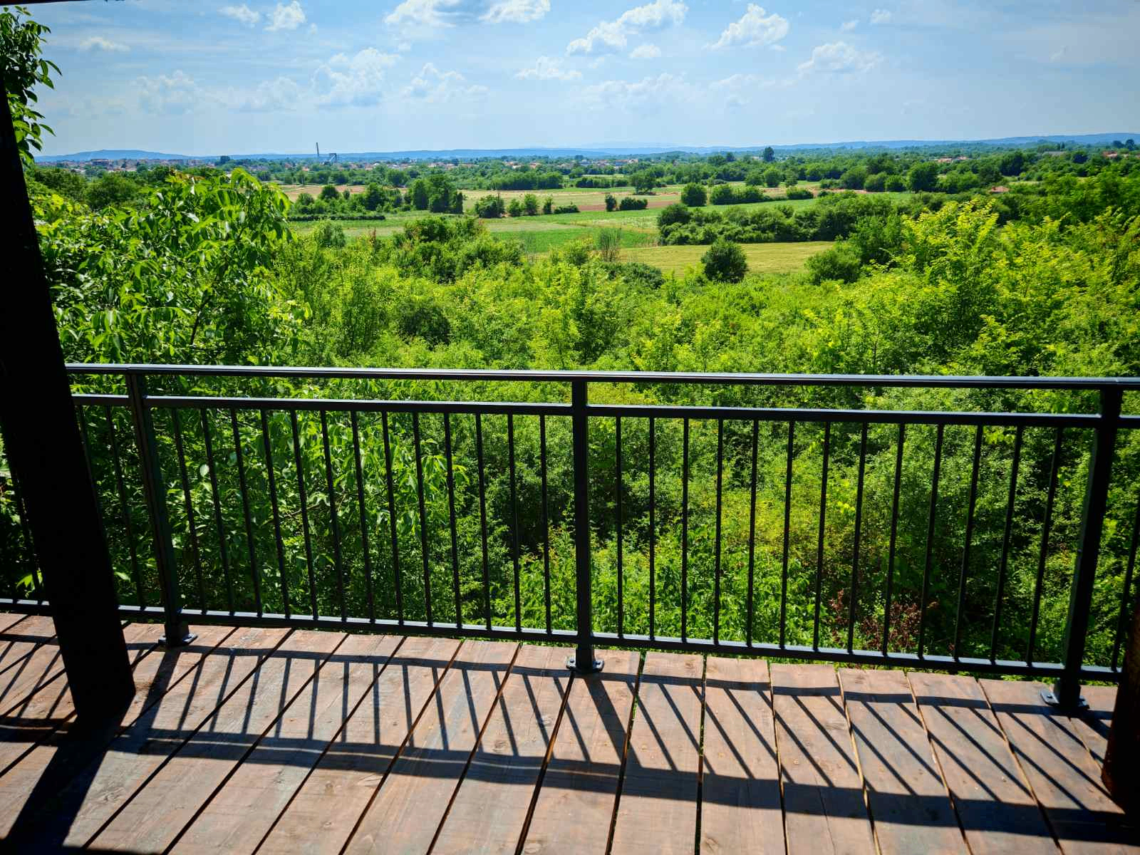 Crni balkon gelender sa pogledom na zelenilo i polja u pozadini